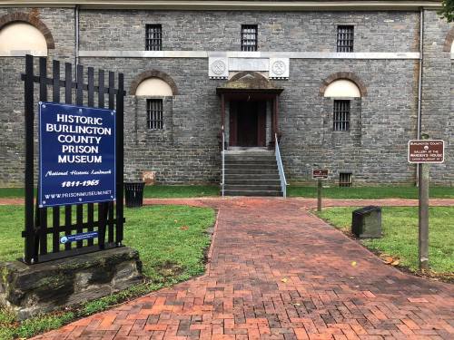 Historic Burlington County Prison Museum entrance with stone building, brick pathway, and informational signs.