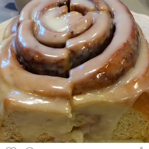 A close-up of a cinnamon roll topped with creamy icing, showcasing its spiral layers and soft texture.