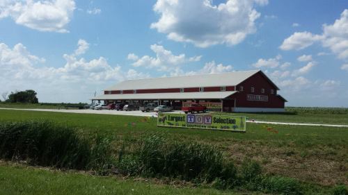 A red barn-style building with a sign advertising "Largest Toy Selection" under a blue sky with fluffy clouds.
