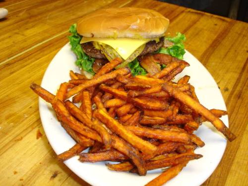 A plate with a cheeseburger topped with lettuce and a side of crispy sweet potato fries.