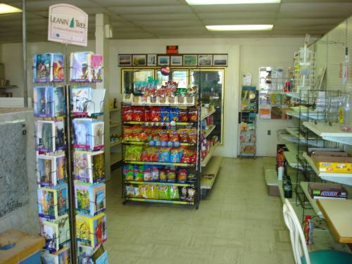 Interior of a small store featuring snack shelves, greeting cards, and a display of various products.