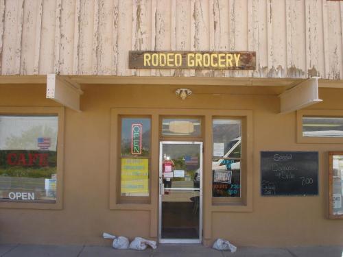 Exterior of Rodeo Grocery with a wooden sign, open door, and chalkboard menu. Bags are placed at the entrance.