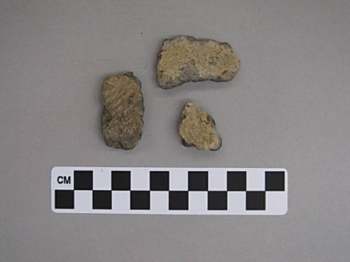 Three pieces of rock on a gray background, with a black and white scale marker below them.