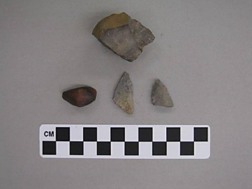 Four stone artifacts displayed on a gray background, with a black and white scale marker below them.