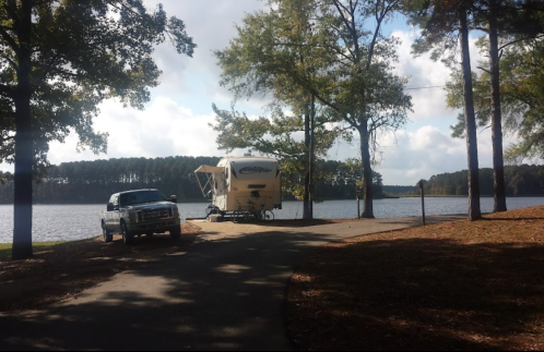 A truck parked near a lakeside campsite with a camper surrounded by trees and a calm water view.