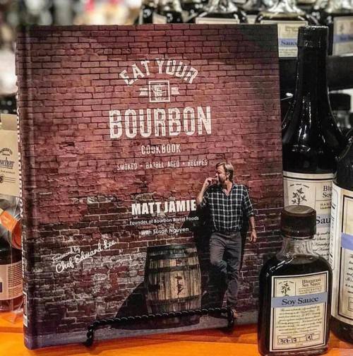 A cookbook titled "Eat Your Bourbon" by Matt Jamie, displayed among various bottles, including soy sauce.