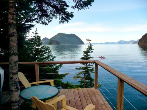 A serene view from a wooden deck overlooking calm waters, mountains in the distance, and a kayak on the lake.