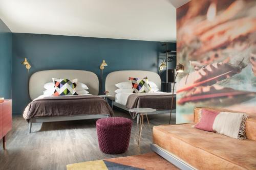 A stylish hotel room featuring two beds, colorful pillows, a cozy seating area, and modern decor.
