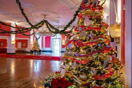 A beautifully decorated Christmas tree with lights and ornaments in a festive room adorned with garlands and red accents.