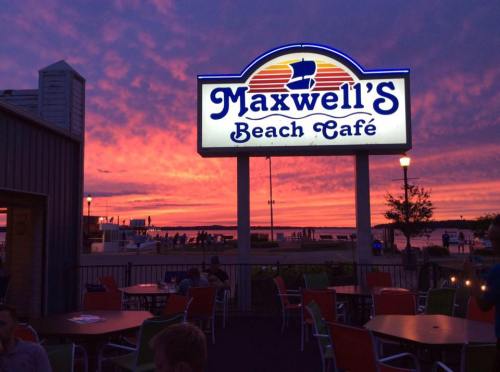 A vibrant sunset over a beach café sign, with colorful clouds and outdoor seating visible in the foreground.