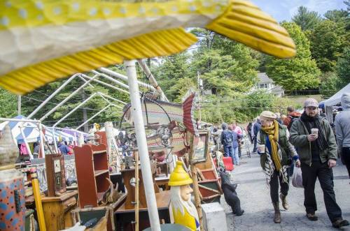 A bustling outdoor market with vintage items, people browsing, and colorful decorations in a scenic setting.