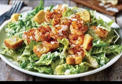 A fresh Caesar salad topped with seasoned shrimp, croutons, and grated cheese on a white plate.