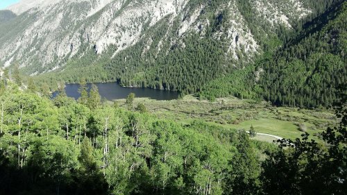 A scenic view of a lush green valley with a lake surrounded by mountains and dense forest.