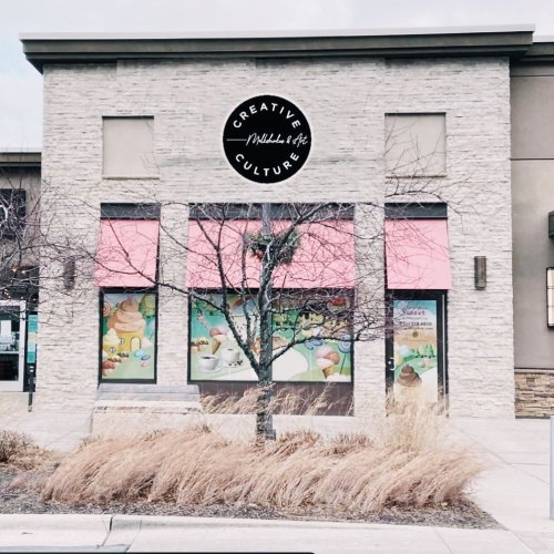 A storefront with a stone facade and pink awnings, featuring colorful window displays and a sign reading "Creative Culture."