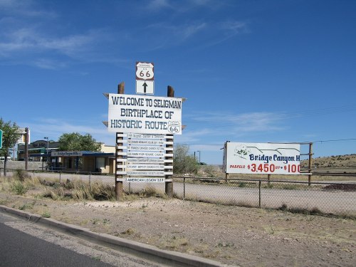 Sign welcoming visitors to Seligman, Arizona, the birthplace of Historic Route 66, with nearby advertisements.