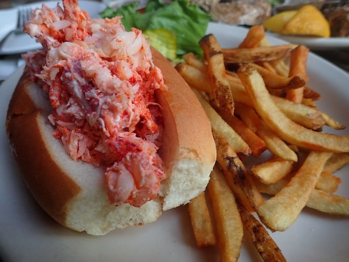 A lobster roll filled with lobster meat, served with a side of golden French fries on a white plate.