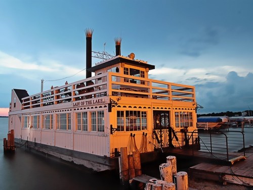 A white paddleboat named "Lady of the Lake" docked on a calm lake under a twilight sky.