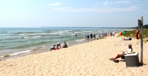 A sandy beach with people enjoying the water, playing, and relaxing under a clear sky.