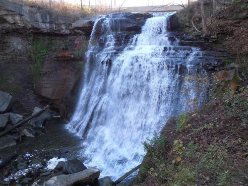 A cascading waterfall flows over rocky cliffs, surrounded by trees and autumn foliage.