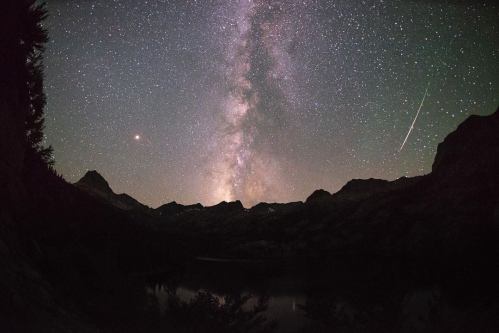 A stunning night sky filled with stars and the Milky Way, framed by mountain silhouettes and a shooting star.