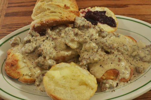 A plate of biscuits topped with creamy sausage gravy, served with a buttered biscuit and a dollop of jam.