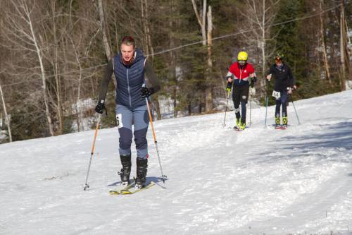 Three skiers ascend a snowy slope, surrounded by trees, enjoying a sunny winter day.