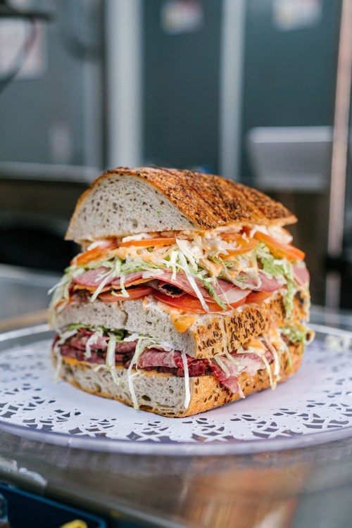 A towering sandwich stacked with layers of meats, vegetables, and bread, served on a decorative plate.