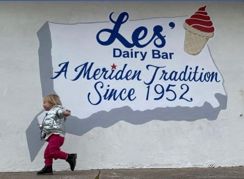 A child walks past a mural of Les' Dairy Bar, featuring an ice cream cone and the text "A Meriden Tradition Since 1952."