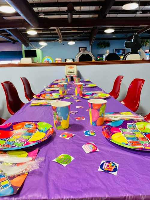 A colorful party table set with vibrant plates, cups, and decorations in a fun indoor space.