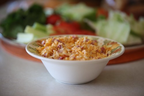 A bowl of shredded cheese sits on a table, with a fresh salad in the background.