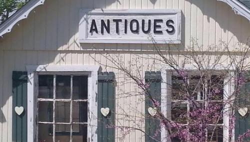 A quaint building with a sign reading "ANTIQUE," featuring green shutters and a tree with pink blossoms.