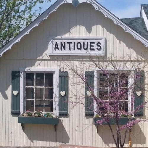 A quaint building with a sign reading "Antiques," surrounded by greenery and blooming flowers.
