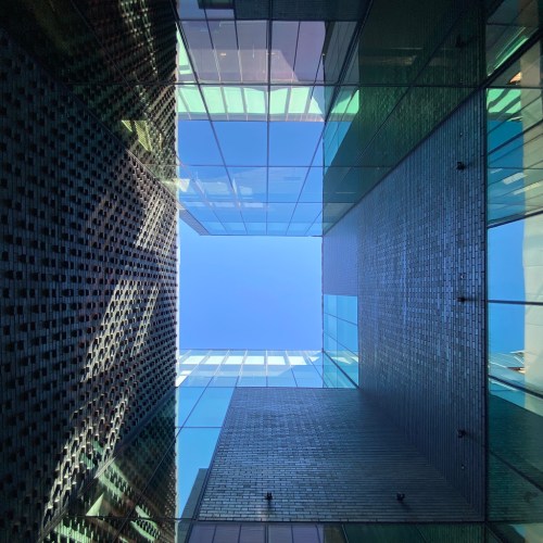 Looking up at a modern building's glass and brick facade, framed by a clear blue sky.