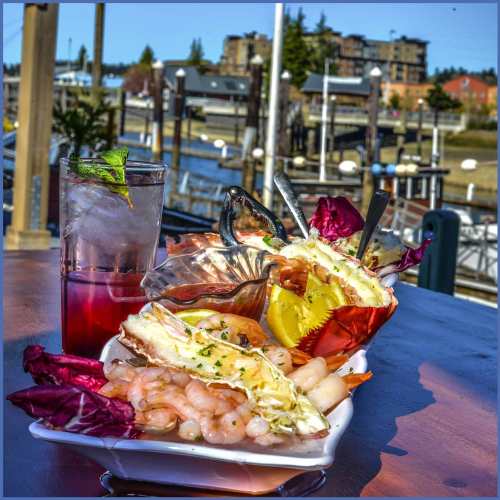 A seafood platter with shrimp and crab, accompanied by two colorful drinks, set against a marina backdrop.