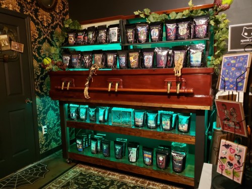 A wooden display resembling a coffin holds colorful bags of tea, surrounded by green lighting and Halloween decorations.