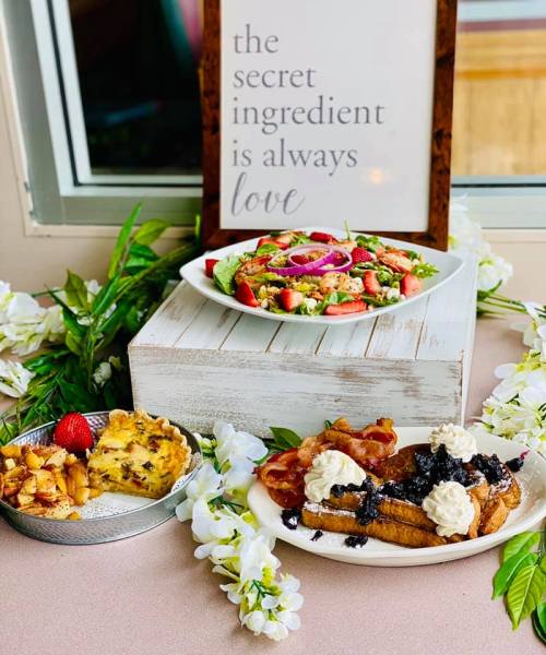A table display featuring a salad, a plate of waffles with toppings, and a sign that reads, "The secret ingredient is always love."