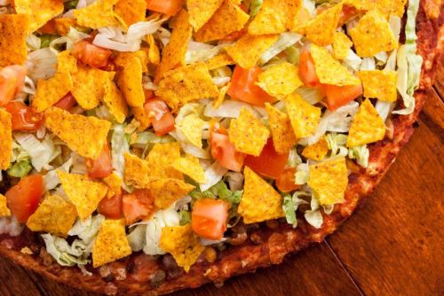 A close-up of a pizza topped with lettuce, diced tomatoes, and crunchy tortilla chips.