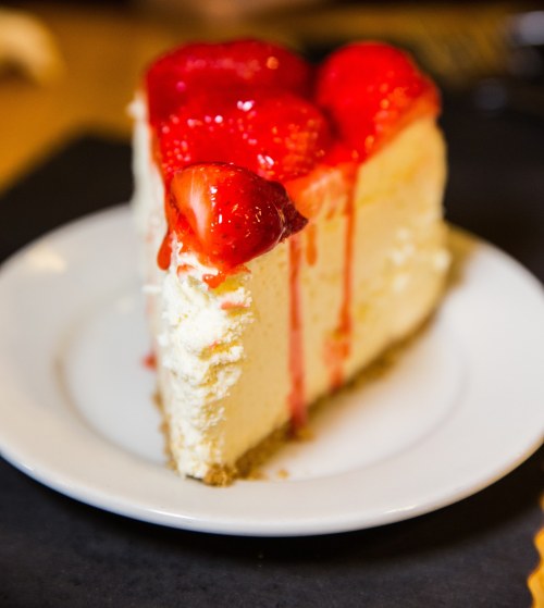 A slice of cheesecake topped with fresh strawberries and strawberry sauce, served on a white plate.