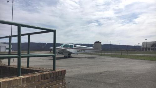 A small airplane parked on a tarmac with a cloudy sky and mountains in the background.