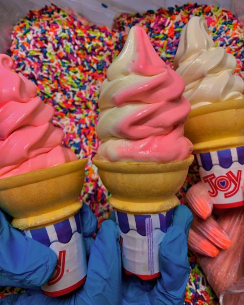 Three ice cream cones with pink and vanilla swirls, held by gloved hands, surrounded by colorful sprinkles.