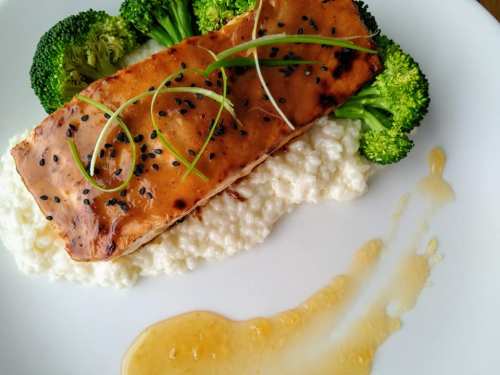 Grilled salmon on a bed of creamy rice, garnished with broccoli and drizzled with sauce.