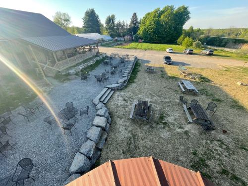 Aerial view of an outdoor seating area with tables and chairs, surrounded by gravel and greenery, under a clear sky.