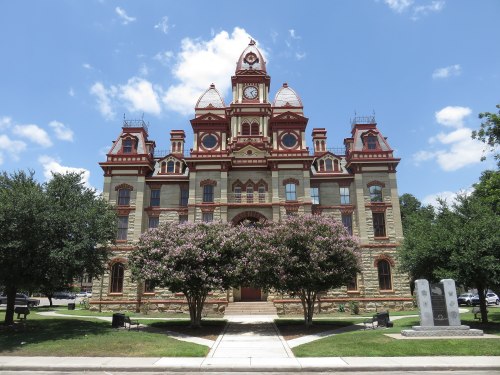 Historic building with ornate architecture, clock tower, and lush trees in front under a blue sky with clouds.