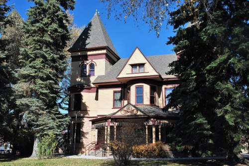 A large, ornate Victorian-style house with a turret, surrounded by trees and a clear blue sky.