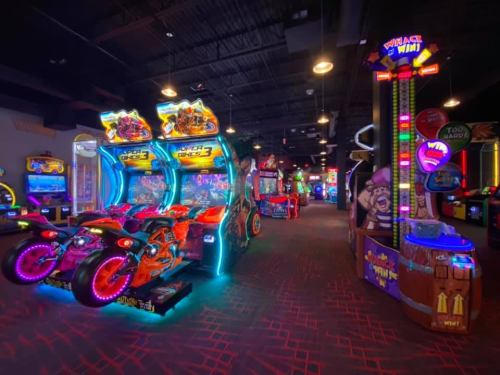 A vibrant arcade filled with colorful games, including motorcycle racing and a prize redemption area.