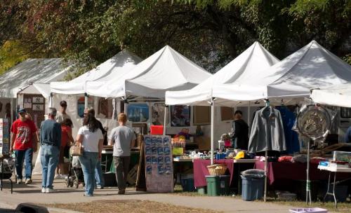 People browsing stalls at an outdoor market with white tents and various goods displayed.