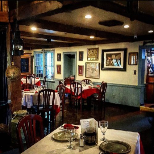Cozy restaurant interior with wooden beams, red tablecloths, and framed artwork on the walls.