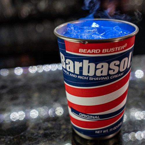 A cup resembling a Barbasol shaving cream can, filled with ice and emitting steam, on a reflective surface.