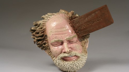 A sculpted head with a beard, eyes closed, and a wooden block labeled "Graveson" striking the top.