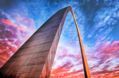 A towering arch structure against a vibrant sunset sky with colorful clouds.